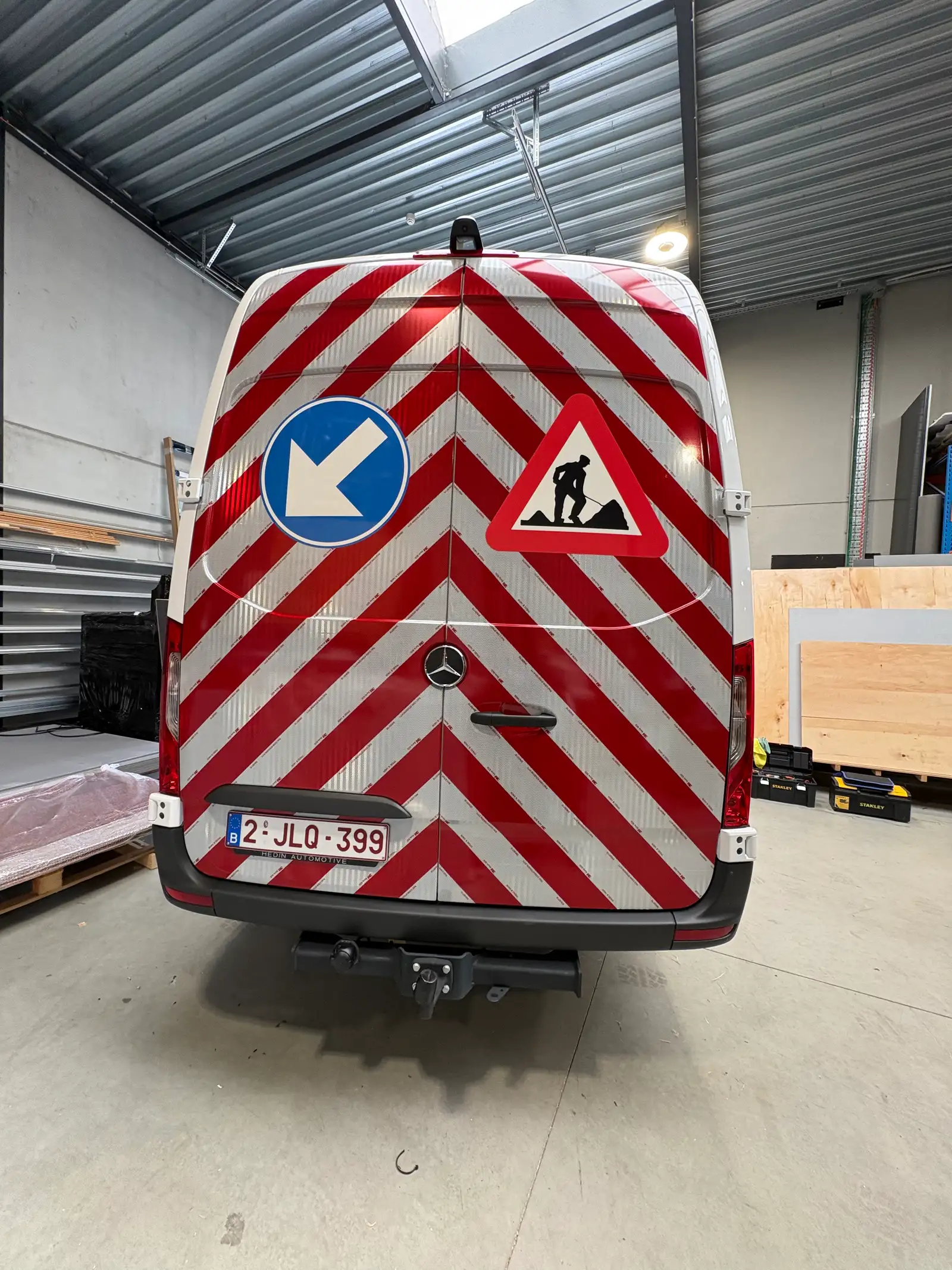 Achterkant van een werfcamionette volledig beletterd met reflecterende rood-witte chevronfolie en verkeersbord-stickers